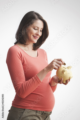 Photo: Pregnant Caucasian woman putting money into piggy bank Pregnant Caucasian woman putting money into piggy bank