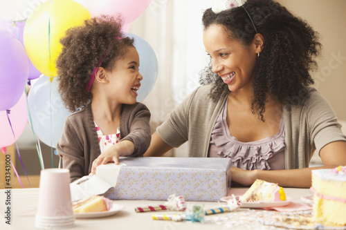 Photo: Mixed race mother watching daughter opening birthday present Mixed race mother watching daughter opening birthday present