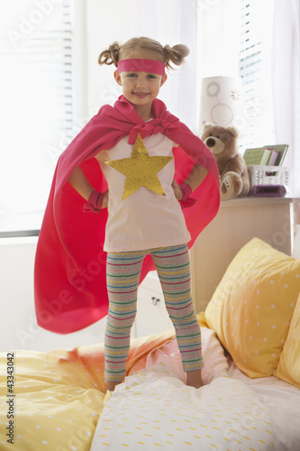 Photo: Caucasian girl dressed as superhero playing on bed Caucasian girl dressed as superhero playing on bed