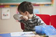 Caucasian boy blowing nose in classroom