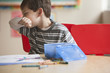 Caucasian boy blowing nose in classroom