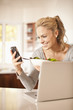 Hispanic woman eating salad and holding cell phone