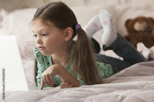 Photo: Caucasian girl laying on bed using laptop Caucasian girl laying on bed using laptop