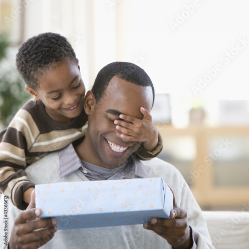 Photo: African American boy covering father's eyes and giving him a gift African American boy covering father's eyes and giving him a gift