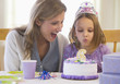 Mother watching daughter blowing out birthday candle
