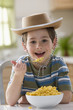 Caucasian boy eating macaroni and cheese and wearing cowboy hat