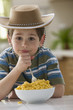 Caucasian boy eating macaroni and cheese and wearing cowboy hat