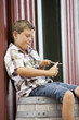 Caucasian boy sitting on barrel whittling stick