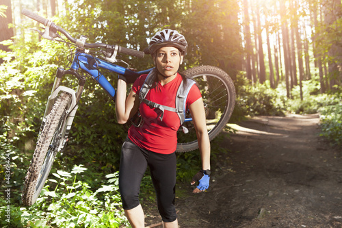Photo: Hispanic woman carrying mountain bike in forest Hispanic woman carrying mountain bike in forest