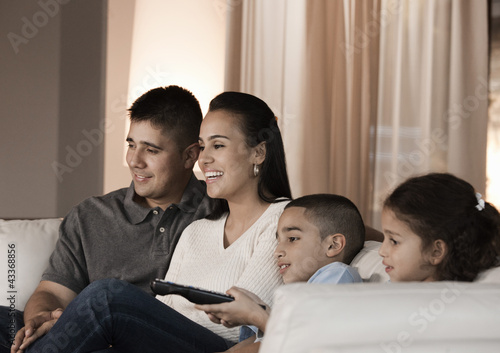 Photo: Hispanic family sitting on sofa watching television Hispanic family sitting on sofa watching television