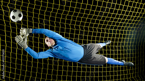 Photo: Caucasian soccer goalie jumping in mid-air catching ball at night Caucasian soccer goalie jumping in mid-air catching ball at night