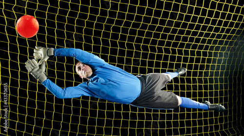 Photo: Caucasian soccer goalie jumping in mid-air catching ball at night Caucasian soccer goalie jumping in mid-air catching ball at night