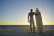 Mixed race man standing on beach with surfboard