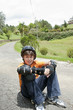 Hispanic boy in pads and helmet sitting on skateboard