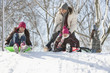 Father and daughters sledding on snow covered hill