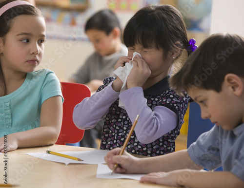 Photo: Mixed race girl blowing nose in classroom Mixed race girl blowing nose in classroom