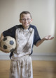 Dirty Caucasian boy holding soccer ball
