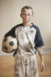 Dirty Caucasian boy holding soccer ball