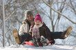 Father and daughter sledding on snow covered hill