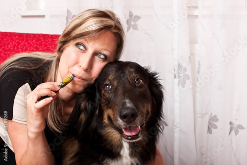 Foto: Junge blonde Frau mit Mischlings Hund dampft E Zigarette Junge blonde Frau mit Mischlings Hund dampft E Zigarette