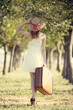 Redhead girl with suitcase at tree's alley.