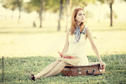 Photo: Redhead girl sitting at bag at outdoor. Redhead girl sitting at bag at outdoor.