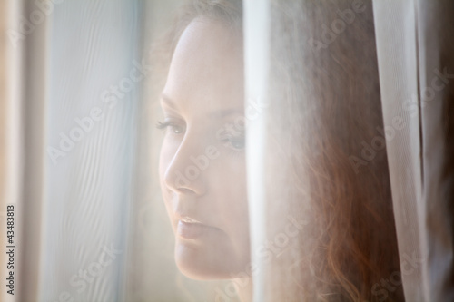 Photo: Sad beautiful woman looking through the window Sad beautiful woman looking through the window