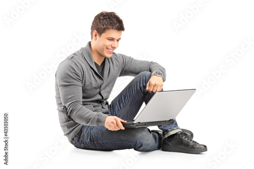 Photo: Handsome guy working on a laptop and sitting on the floor Handsome guy working on a laptop and sitting on the floor