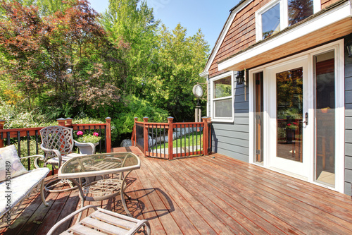 Photo: House exterior with large open deck with outdoor furniture. House exterior with large open deck with outdoor furniture.