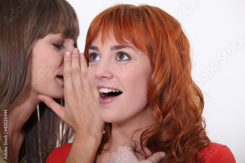 Photo: Woman whispering into another woman's ear Woman whispering into another woman's ear