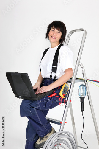 Foto: Female electrician sat on ladder with laptop Female electrician sat on ladder with laptop