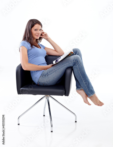 Photo: Beautiful young girl sitting in a chair with magazine Beautiful young girl sitting in a chair with magazine