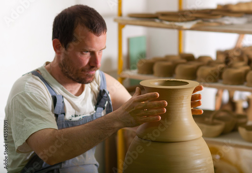 Photo: Craftsman making vase from fresh wet clay on pottery wheel Craftsman making vase from fresh wet clay on pottery wheel