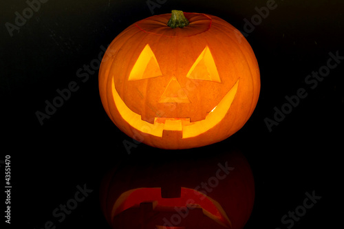 Photo: Halloween pumpkin with scary face with reflection on black glass Halloween pumpkin with scary face with reflection on black glass