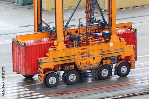 Foto: Large loader drives on wet asphalt and carries red container Large loader drives on wet asphalt and carries red container