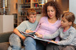 Son and daughter with their mother sit on sofa and read book