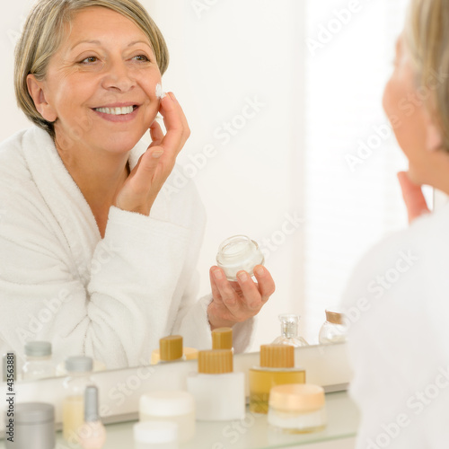 Photo: Senior woman apply anti-wrinkles cream look mirror Senior woman apply anti-wrinkles cream look mirror