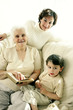 Photo : A young boy sitting with his grandmother and mother on the couch looking at the camera A young boy sitting with his grandmother and mother on the couch looking at the camera