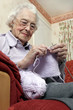An old bespectacled woman sitting on the couch knitting