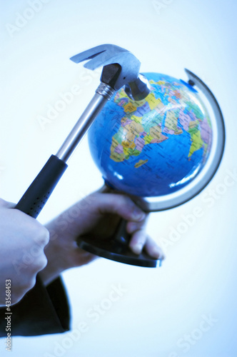 Photo: Portrait of a hand holding a hammer trying to break a globe Portrait of a hand holding a hammer trying to break a globe