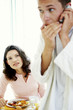 A man whispering on the hand phone as his wife watching suspiciously