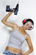 A woman with goggles and headphone raising a driller above her head