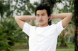 A man leaning against a tree on a lakeside with his hands behind his head