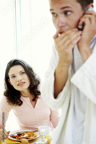 Photo: A man whispering on the hand phone as his wife watching suspiciously A man whispering on the hand phone as his wife watching suspiciously