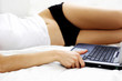 Chest down shot of a woman lying on the bed with a laptop by her side