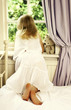 Back shot of a girl peeking out from the bedroom window