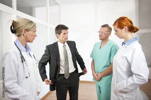 Photo: Businessman showing empty pockets to doctors Businessman showing empty pockets to doctors