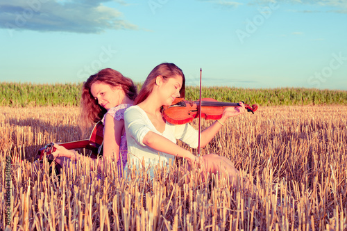 Photo: Two young women playing guitar and violin outdoors. Split toning Two young women playing guitar and violin outdoors. Split toning