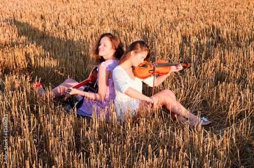Photo: Two young women playing guitar and violin outdoors Two young women playing guitar and violin outdoors