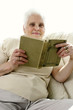 An old lady sitting on the couch reading a book